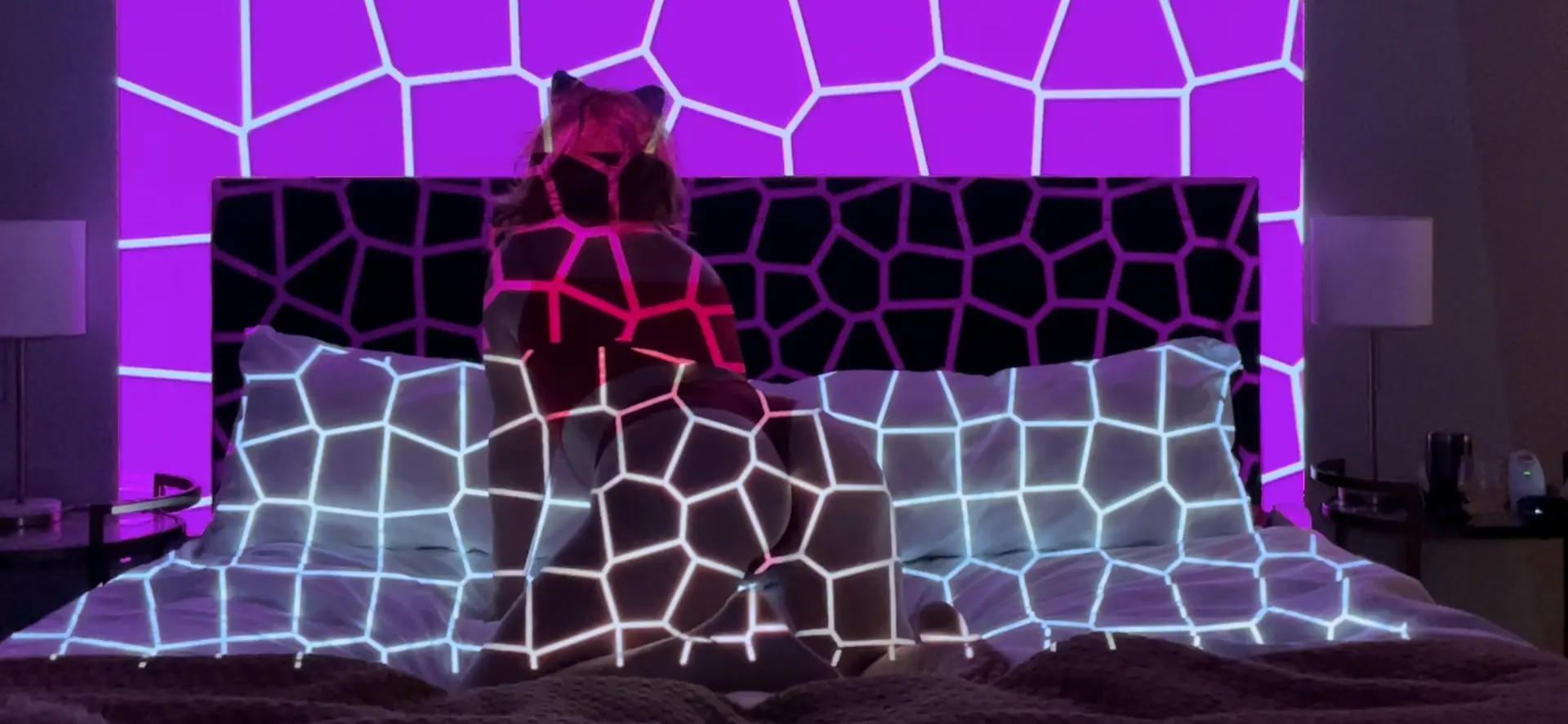 Violet and cyan cellular light patterns projected across a bed and headboard