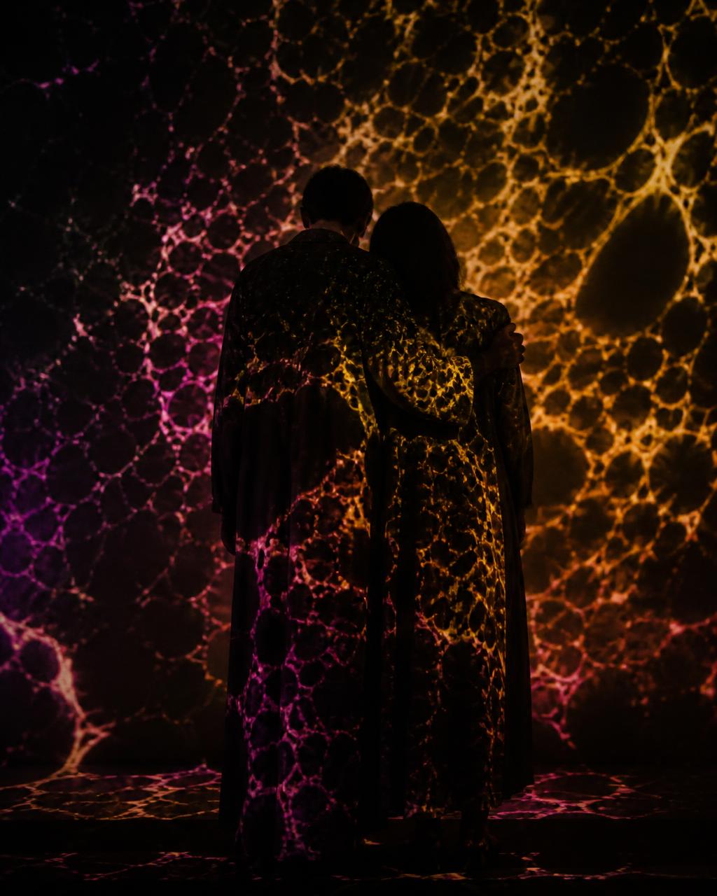 Two figures silhouetted against a bold projected pattern of coloured geometric shapes